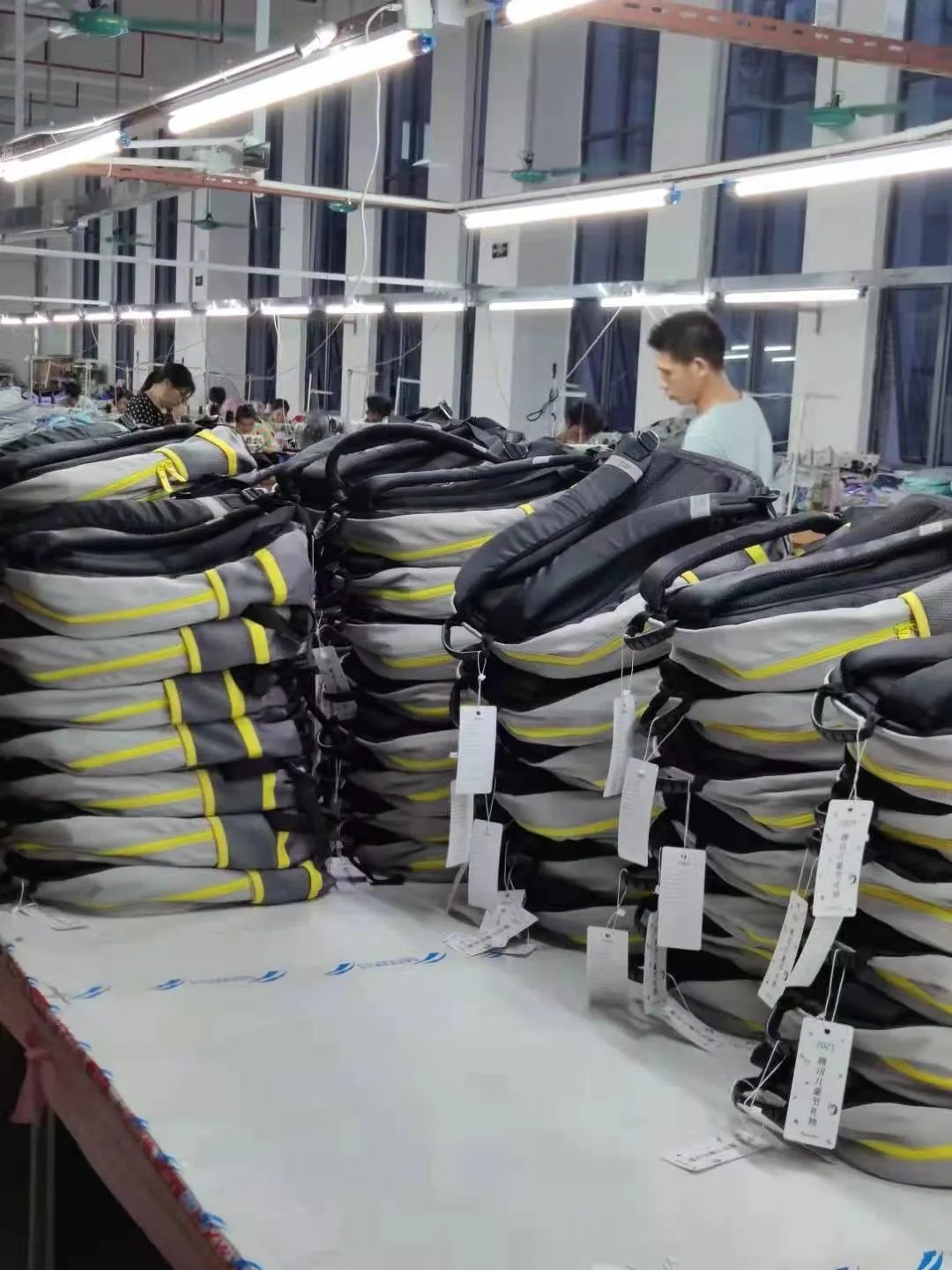 Male QC inspector checking labeled black and grey Custom Backpacks in a Manufacturer factory.