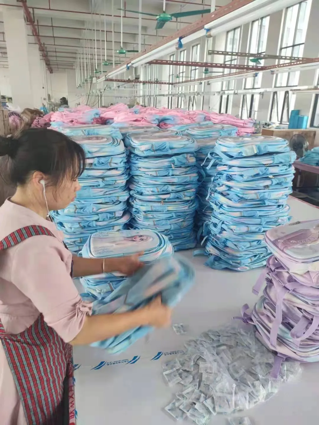Female worker organizing blue and pink Bulk Backpacks. Children's bag OEM Manufacturing process.