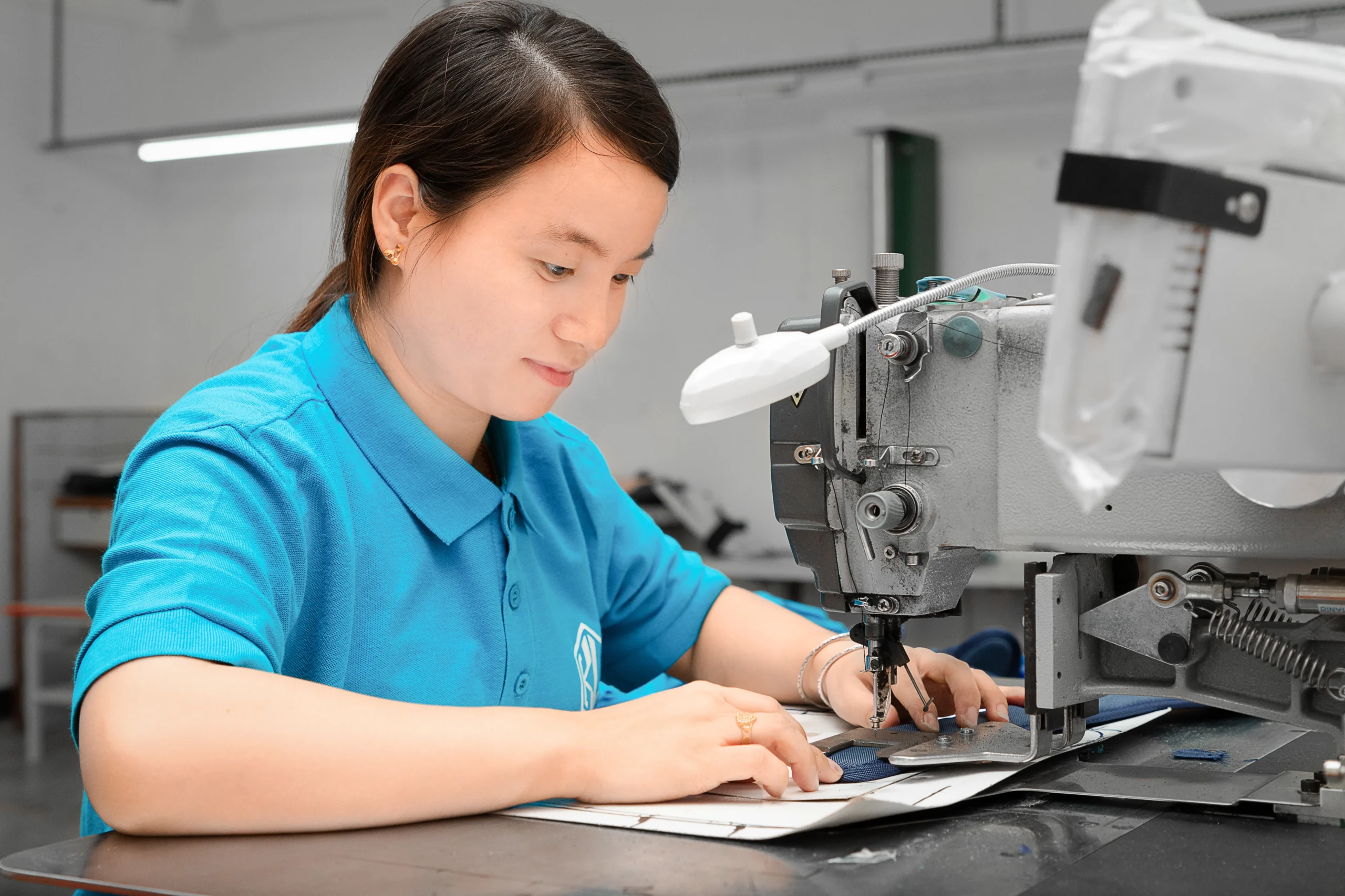 Female worker sewing blue fabric on an industrial machine. Expert craftsmanship at a Backpack OEM Manufacturer factory.