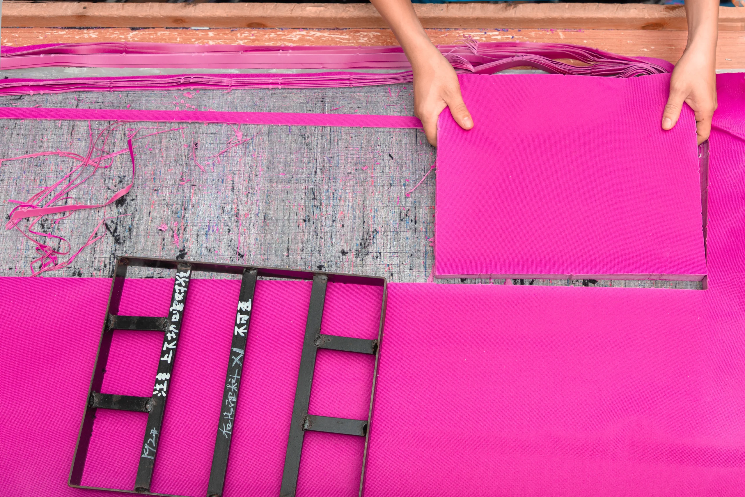 Hands stretching and arranging pink fabric on a cutting table. Material handling at a Backpack OEM Supplier.
