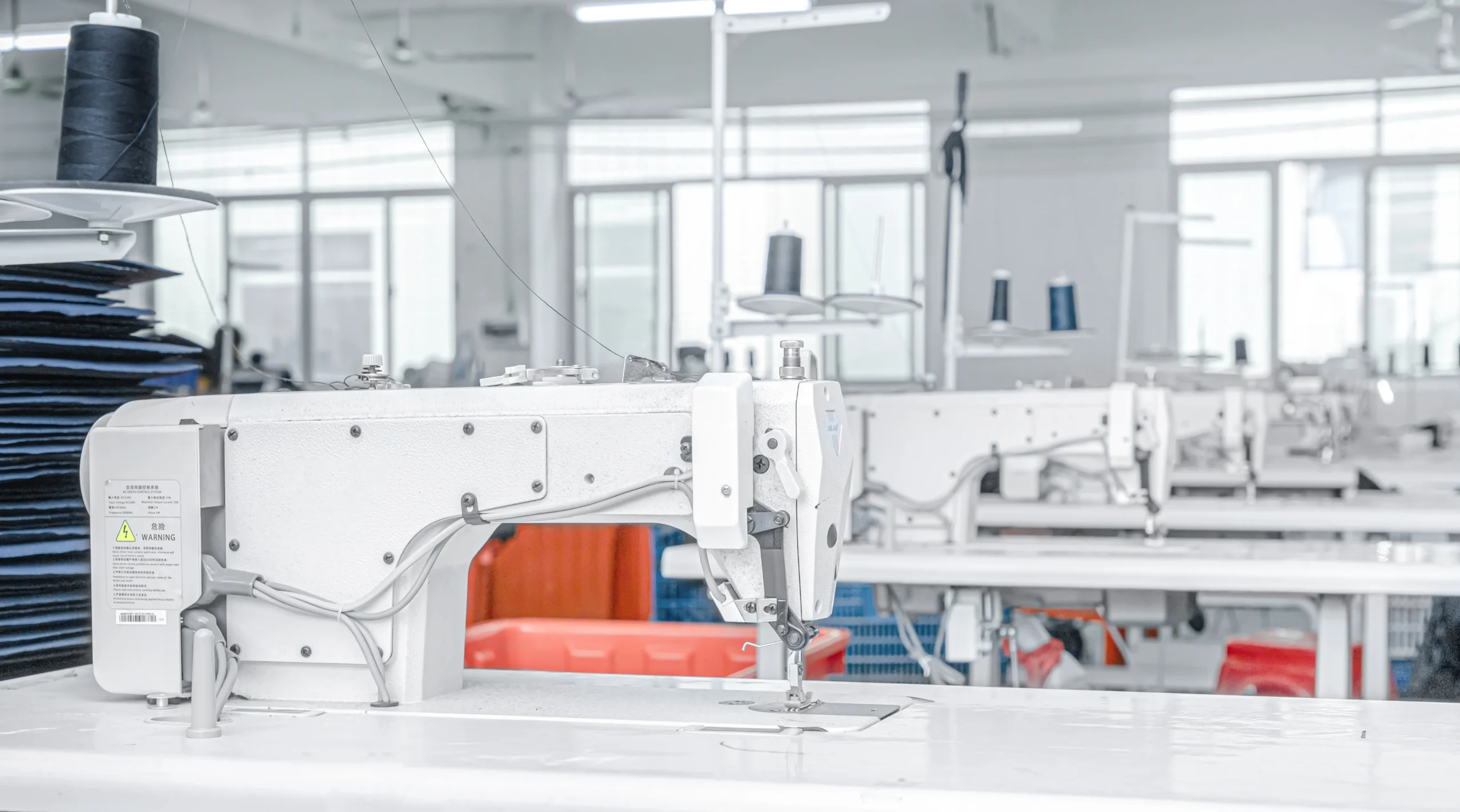 A row of industrial sewing machines in a bright factory. The production line of a Backpack OEM Supplier.