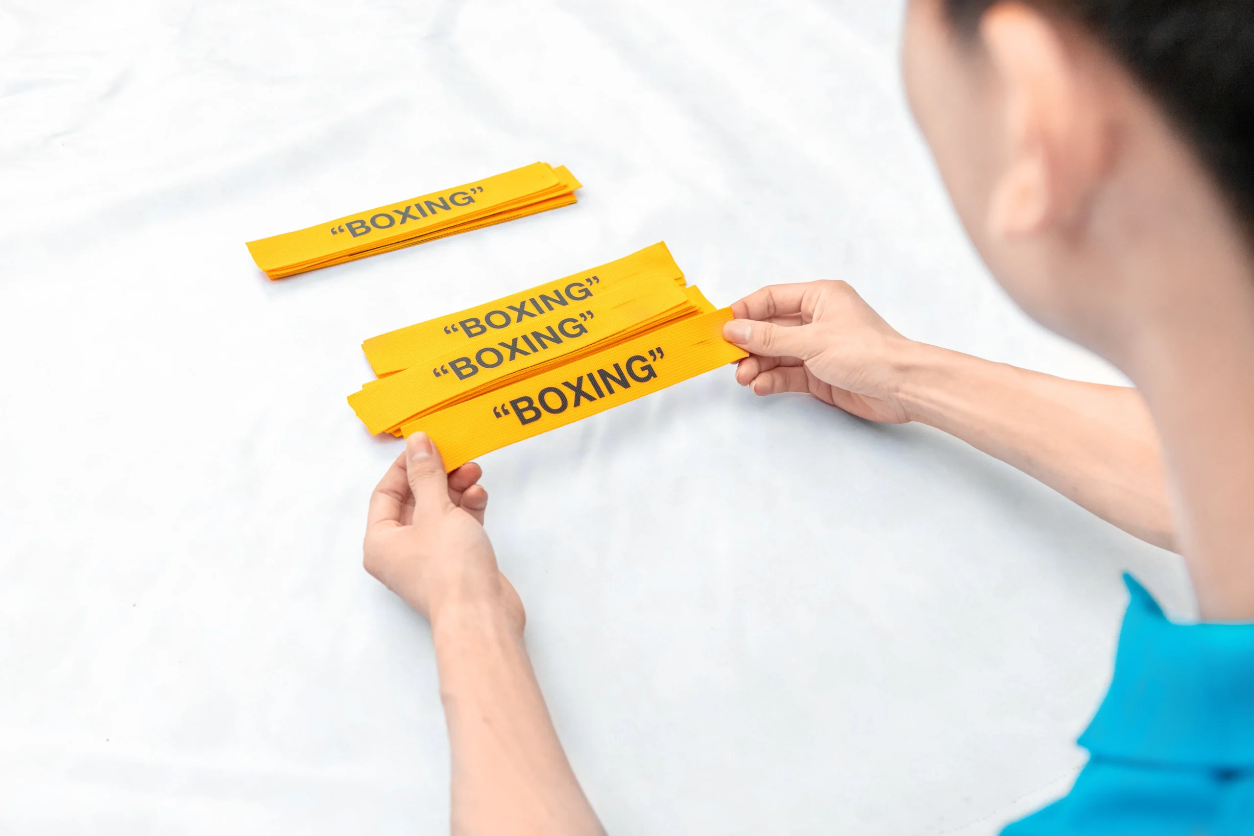 Hands sorting yellow "BOXING" print labels. Custom branding materials by a Backpack OEM Manufacturer.