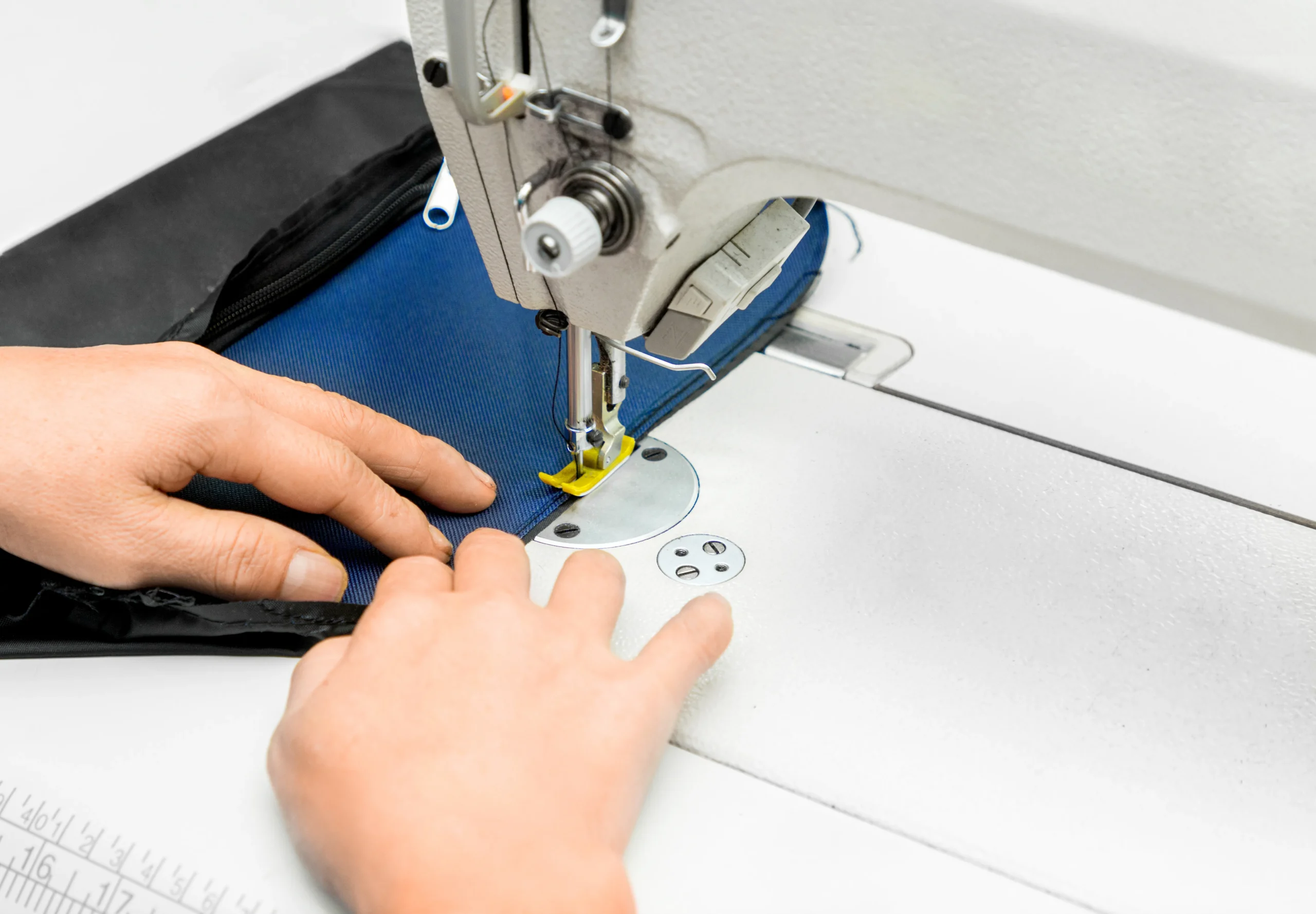 Close-up of stitching blue fabric onto a black backpack. Precision sewing at a leading Backpack Manufacturer.