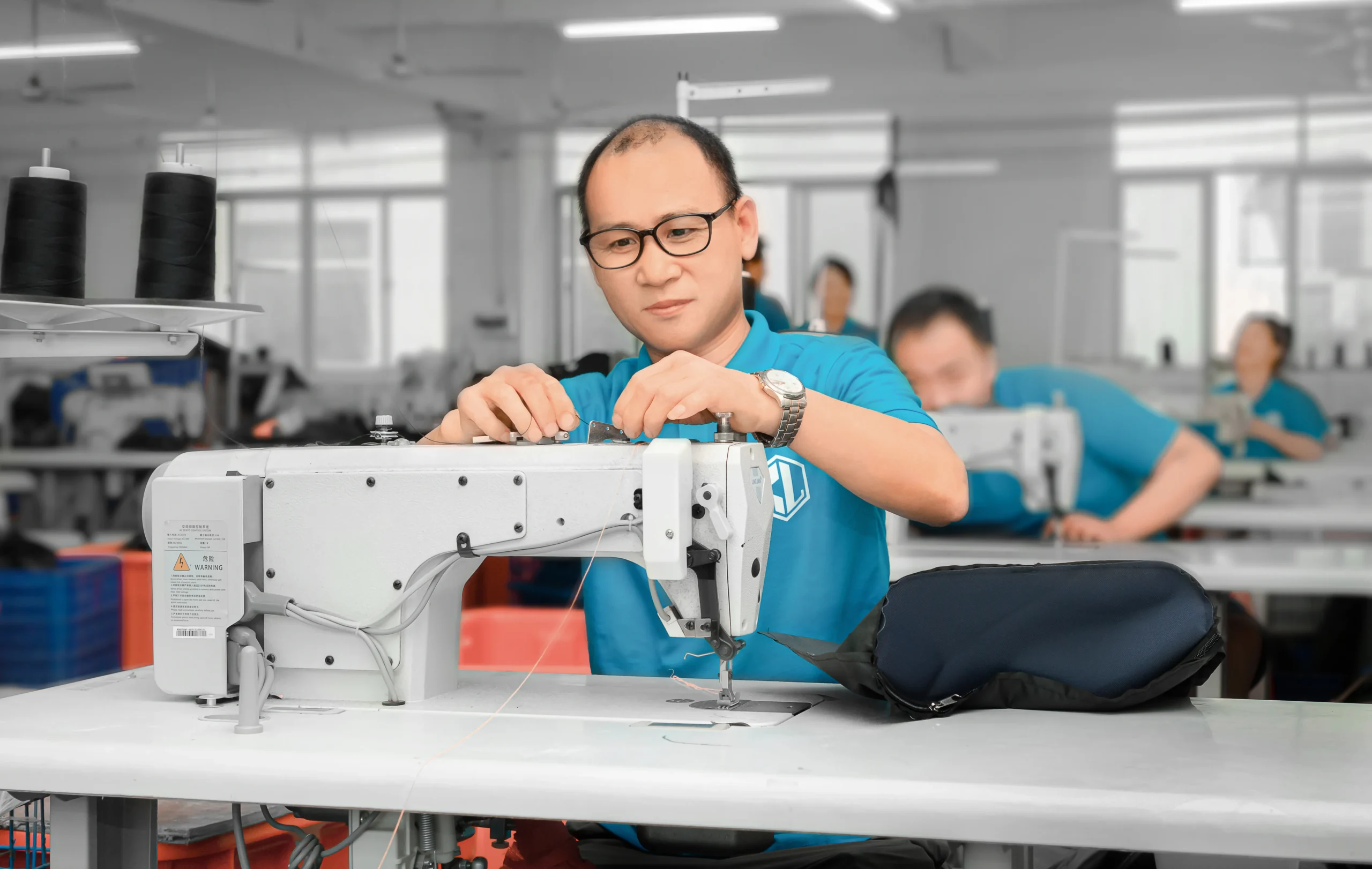 Male worker adjusting a sewing machine for backpack production. Quality equipment maintenance by a leading OEM Supplier.