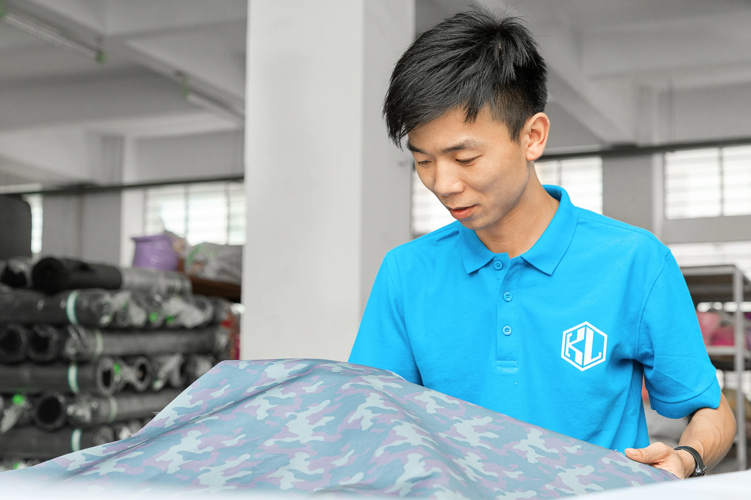 Male QC worker inspecting a roll of camouflage fabric. Raw material quality check at a Backpack OEM Supplier.