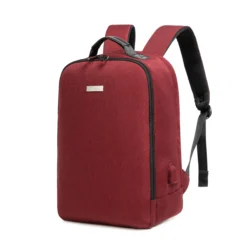 Slanted front view of a minimalist burgundy business backpack with a sleek silver logo plate and a side charging port. Functional smart backpack by a Custom Backpack Manufacturer.