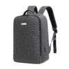 Slanted front view of a minimalist dark grey business backpack with a sleek silver logo plate and a side charging port. Functional smart backpack by a Custom Backpack Manufacturer.