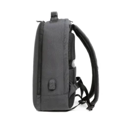 Side profile of a minimalist dark grey backpack showing its slim profile, luggage strap, and side charging port. Travel-friendly bag by a Backpack OEM Supplier.