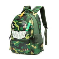 Slanted front view of a cool kids' backpack featuring a 3D monster face with big teeth, a yellow fin, and a green monster keychain. Fun school bag by a Backpack Manufacturer.
