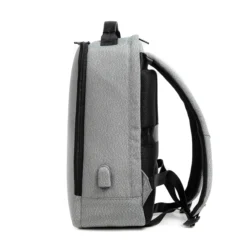 Side profile of a minimalist light grey backpack showing its slim profile, luggage strap, and side charging port. Travel-friendly bag by a Backpack OEM Supplier.