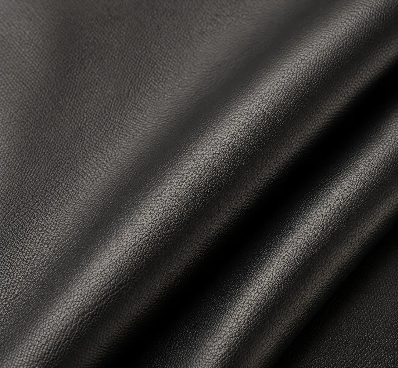Close-up macro shot of a pebbled black leather or synthetic leather fabric, showcasing a classic textured surface. Premium material for custom backpacks by a Backpack Manufacturer Supplier.